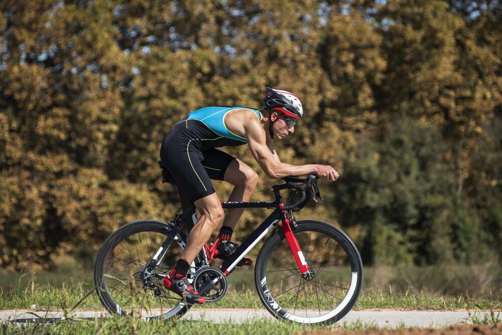 Maschsee Hannover - Ein Radfahrer in blau-schwarzem Outfit rast auf einem rot-schwarzen Rennrad den gepflasterten Weg entlang und verkörpert damit den Geist des Hannover Triathlons. In aerodynamischer Haltung nach vorne gebeugt rasen sie an Bäumen vorbei, die mit leuchtendem Herbstlaub geschmückt sind. - maschseefest Hannover