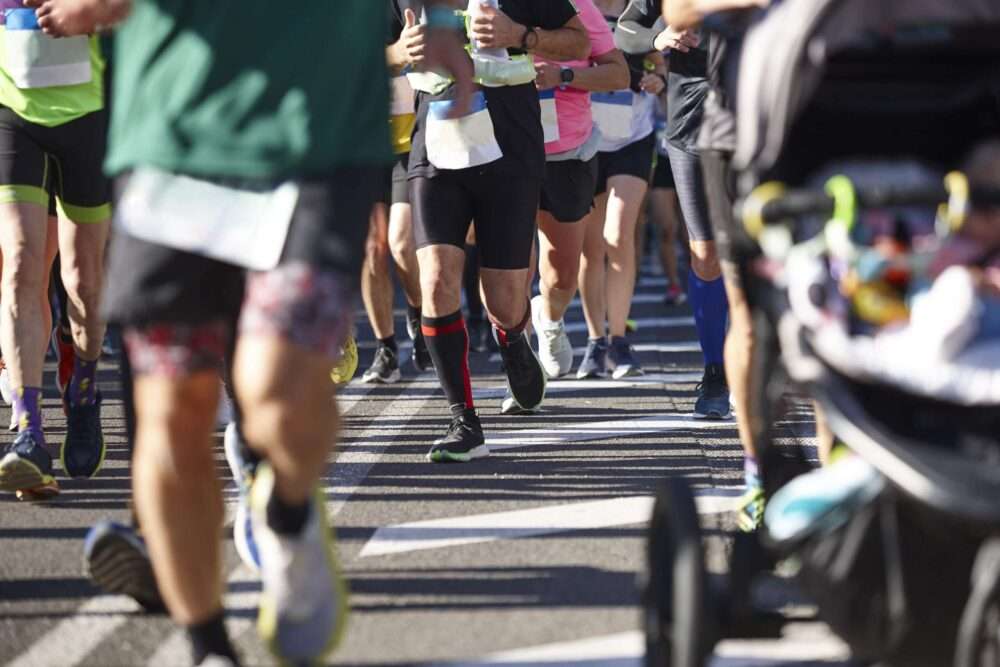 Maschsee Hannover - Eine Gruppe von Läufern beim ADAC Marathon Hannover 2025. Einige Läufer sind mitten im Laufschritt und präsentieren farbenfrohe Sportbekleidung und Schuhe. Auf der rechten Bildseite ist ein Kinderwagen teilweise zu sehen. - maschseefest Hannover