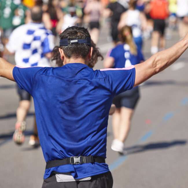 Maschsee Hannover - Inmitten des energiegeladenen Treibens beim ADAC Marathon Hannover 2025 reckt ein Läufer in blauem Shirt und schwarzer Kappe triumphierend die Arme in die Höhe. Er fällt aus der Menge der Teilnehmer auf, die alle in unterschiedlicher Sportkleidung die sonnige Straße entlangrennen. - maschseefest Hannover