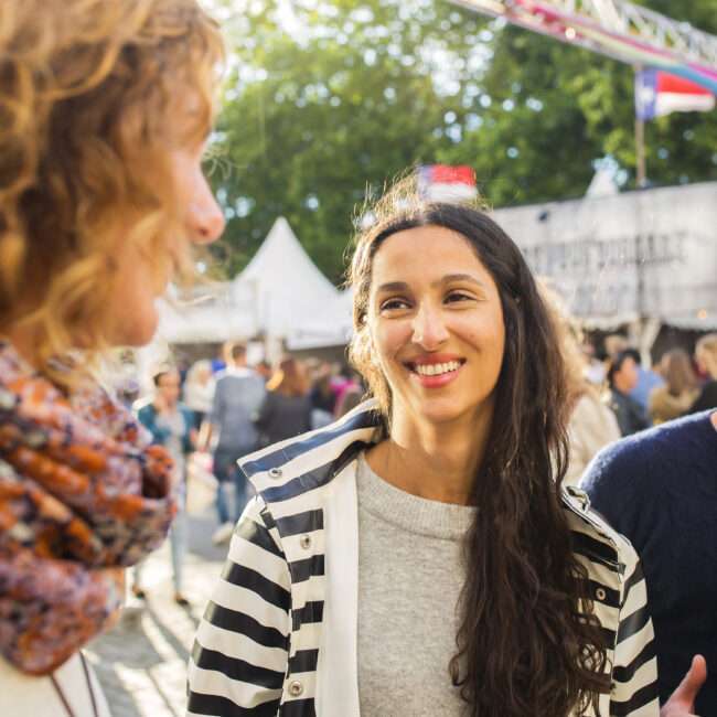 Maschsee Hannover - Bei der Veranstaltung am Maschsee in Hannover unterhalten sich drei Personen. Die Person links ist teilweise zu sehen, während die Personen in der Mitte und rechts sich herzlich anlächeln. Zelte und Bäume bilden an diesem sonnigen Tag eine malerische Kulisse. - maschseefest Hannover