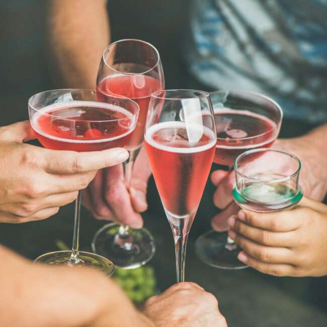 Maschsee Hannover - Fünf Hände heben Gläser mit rosa Cocktails und stoßen inmitten der pulsierenden Energie des Maschseefests Hannover 2025 an. Jedes einzelne Glas fängt das Licht ein und steht vor einem sanft verschwommenen Hintergrund, der dieses fröhliche Beisammensein hervorhebt. - maschseefest Hannover