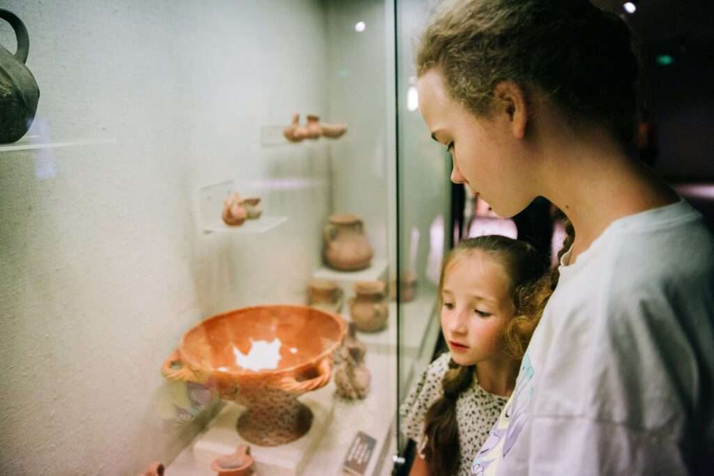 Maschsee Hannover - Zwei junge Menschen betrachten eine Ausstellung antiker Keramik im Museum Hannover. Die Ausstellung ist in einer Glasvitrine untergebracht und zeigt verschiedene Tongefäße. Die Beleuchtung im Inneren hebt die Details der Artefakte hervor, und die Personen wirken interessiert und konzentriert. - maschseefest Hannover