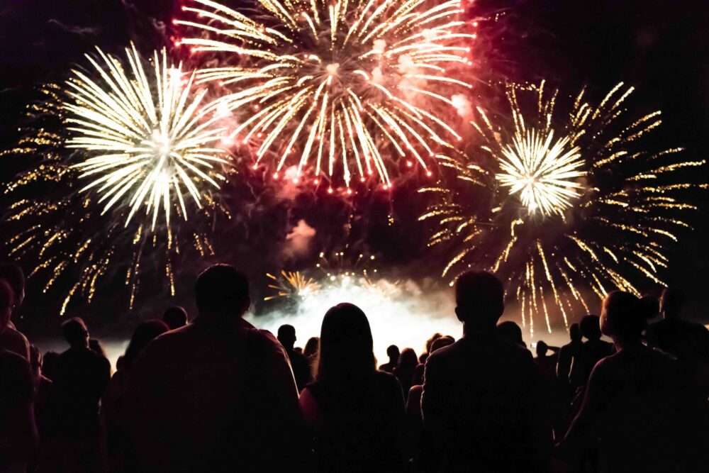 Maschsee Hannover - Eine Gruppe von Menschen zeichnet sich vor dem von leuchtendem Feuerwerk erleuchteten Nachthimmel beim Schützenfest Hannover ab. Zahlreiche rote und goldene Feuerwerkskörper erleuchten den Himmel und schaffen eine festliche und dramatische Szene. Die Menge blickt nach oben und beobachtet das schillernde Spektakel. - maschseefest Hannover