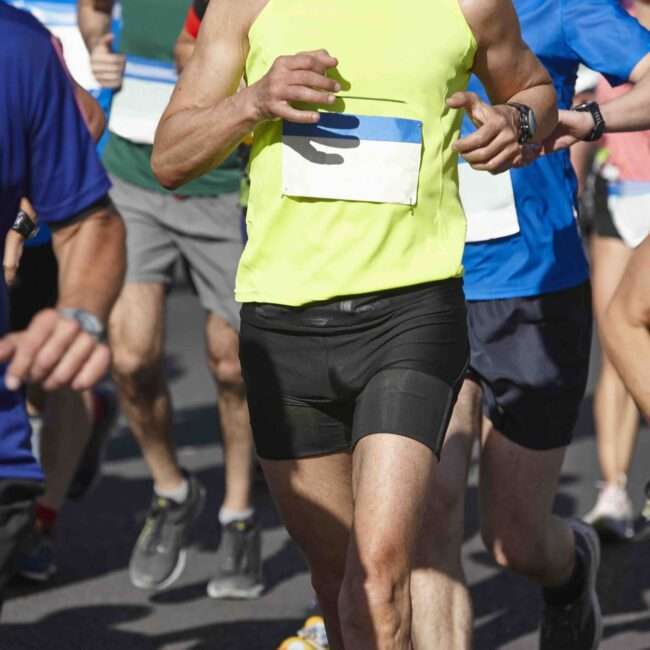 Maschsee Hannover - Mittelteil einer Läufergruppe beim Silvesterlauf Hannover 2025. Sie tragen Sportkleidung, ihre Startnummern sind gut sichtbar an ihren Shirts befestigt. Der Fokus liegt auf ihren Beinen und Oberkörpern, während sie dicht an dicht auf einer asphaltierten Straße laufen und so den Geist der Veranstaltung verkörpern. - maschseefest Hannover