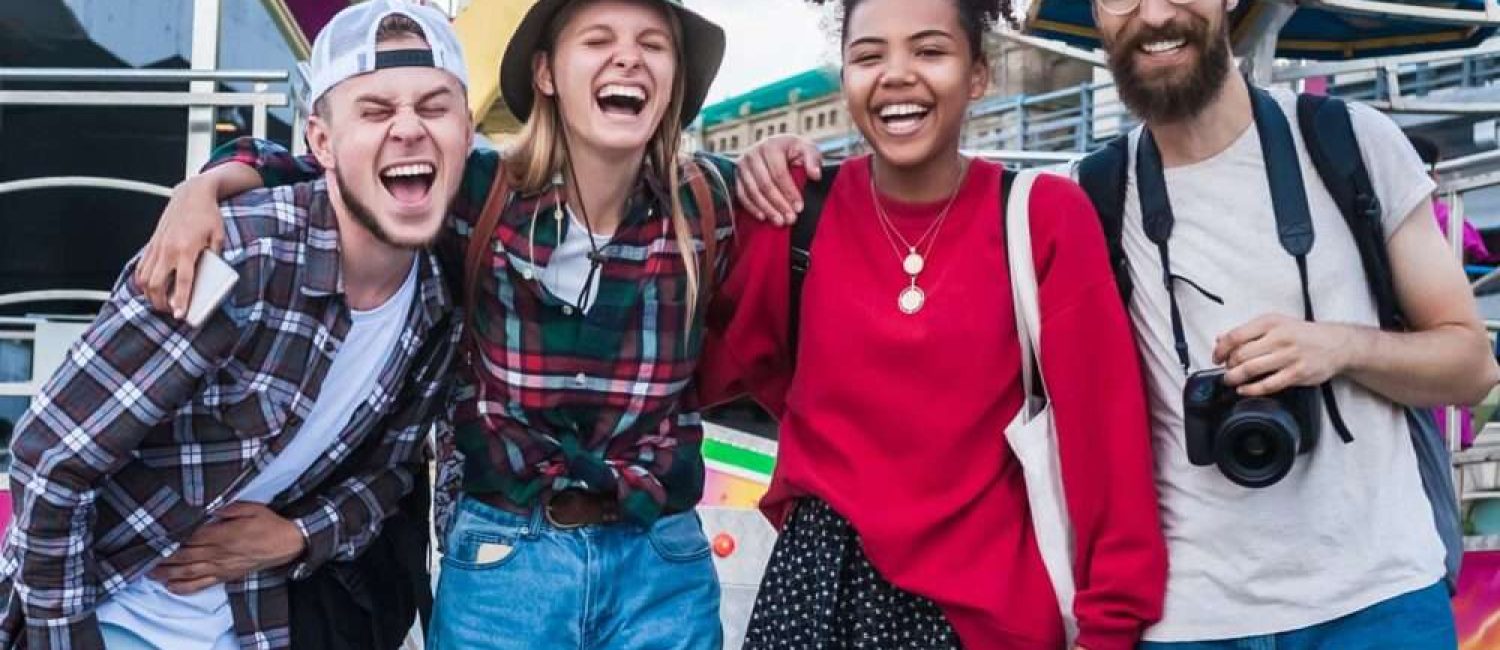 Maschsee Hannover - Vier Freunde stehen lachend dicht beieinander vor einem farbenfrohen Fahrgeschäft auf dem Oktoberfest in Hannover. Drei sind leger gekleidet, tragen Hüte, einer hält eine Kamera in der Hand und hält Erinnerungen inmitten der bunten Attraktionen des Vergnügungsparks fest. - maschseefest Hannover